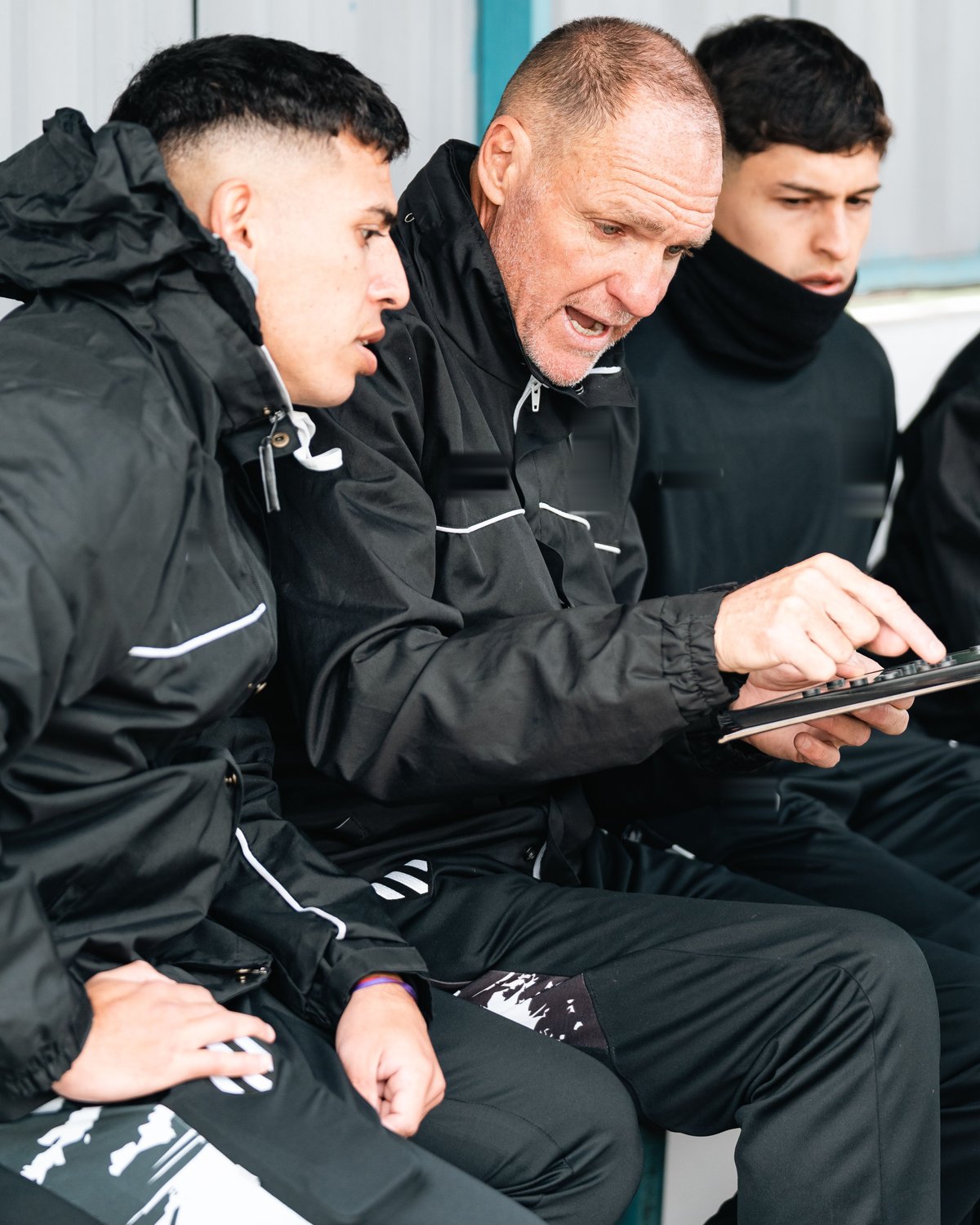 A coach reviewing a match moment on a tablet with two players